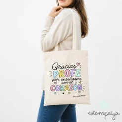 Modelo posando de espaldas con bolsa de tela personalizada gracias profe por enseñarme con el corazón con nombre de alumno.