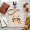 Bolsa Tote de Tela Personalizada "Profe Lápices" - Estampatya Bolsa de tela personalizada para regalo de profesora con diseño de lápices y nombre de alumno sobre mesa decorada.