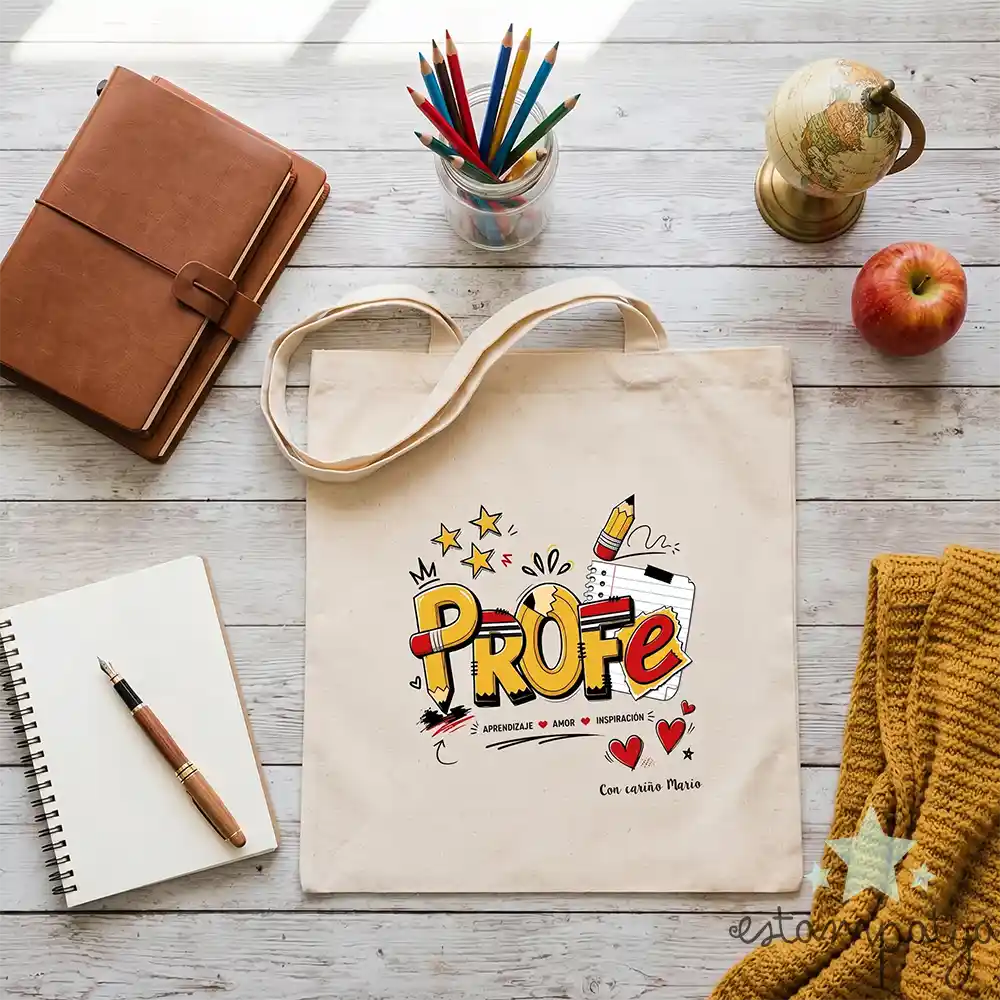 Bolsa Tote de Tela Personalizada "Profe Lápices" - Estampatya Bolsa de tela personalizada para regalo de profesora con diseño de lápices y nombre de alumno sobre mesa decorada.